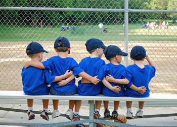 five little boys put their arms around each other before their baseball game