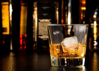 whiskey glass with ice in front of bottles