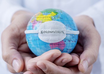 closeup of a caucasian doctor man holding a world globe with a protective mask with the word coronavirus written in it