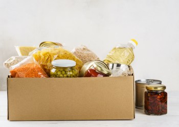 Various canned food, pasta and cereals in a cardboard box.