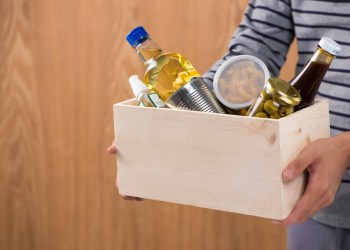 Volunteer with donation box with foodstuffs on wooden background