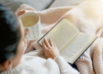 Cosy brunette at home on couch with hot drink and reading