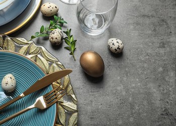 Festive Easter table setting with eggs on color background, above view. Space for text