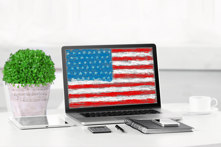 Modern workplace with laptop on table indoors. American flag on screen