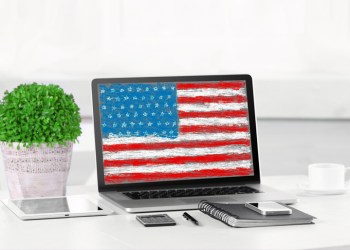 Modern workplace with laptop on table indoors. American flag on screen