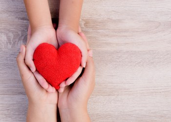 Health care, love, organ donation, family insurance and CSR concept. adult and child hands holding handmade red heart on wooden background.