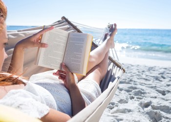 Brunette reading a book while relaxing in the hammock at the beach