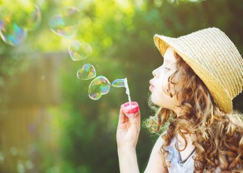 Cute girl blowing soap bubbles in a heart shape.