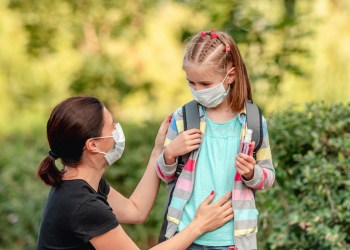 Mother putting mask on daughter before school