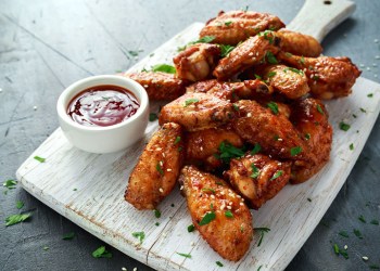 Baked chicken wings with sesame seeds and sweet chili sauce on white wooden board