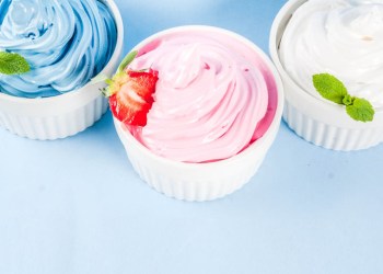 Healthy diet summer dessert, vanilla and berry frozen yogurt or soft ice cream in white bowls, isolated on light blue background copy space