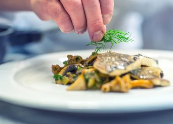 Chef in hotel or restaurant kitchen cooking, only hands. Prepared fish steak with dill decoration