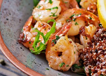 Delicious healthy Buddha bowl with shrimps, tomato, avocado, quinoa, lemon and arugula on the wooden table. Healthy food.