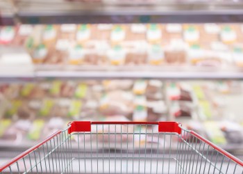 Empty red shopping cart with Abstract fresh meat shelves in supermarket grocery store blurred defocused background with bokeh light