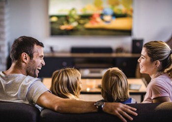Happy parents talking while watching TV with their kids at home.