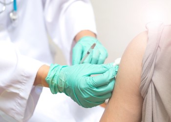 Vaccination healthcare concept. Hands of doctor or nurse in medical gloves injecting a shot of vaccine to a man patient