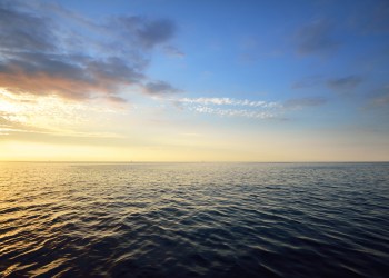 Sunset in a cloudy sky over open Baltic sea with veri distant ship silhouettes.