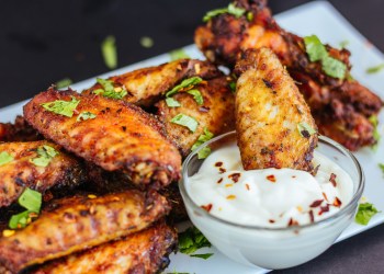 Spicy Chicken Wings with Cilantro, White Sauce and Chili Flakes on White Platter, Dark Background Photo