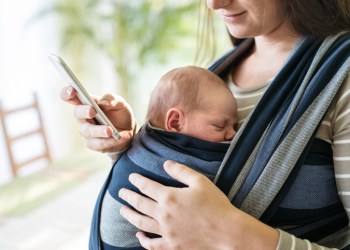 Unrecognizable mother with her son in sling and smartphone