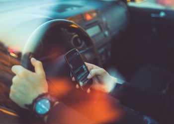 Young businessman driving a car and using smartphone