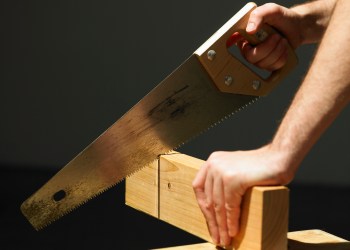 Man cutting through block of wood using saw, close-up of hands