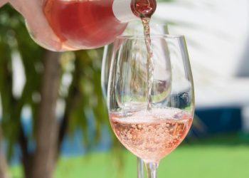 close up of a hand pouring delicious rose wine from bottle into glass outdoors . lifestyle concept