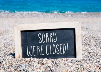 a wooden-framed chalkboard with the text sorry we are closed written in it, placed on the sand of a beach, with the sea in the background