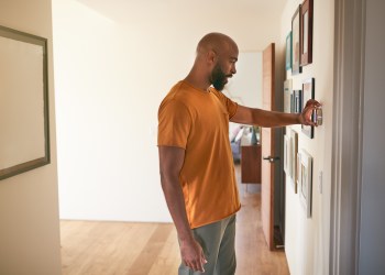 Man Adjusting Digital Central Heating Thermostat At Home