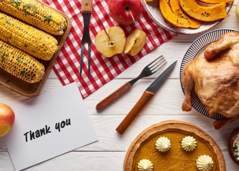 top view of pumpkin pie, turkey and vegetables served at white wooden table with thank you card for Thanksgiving dinner