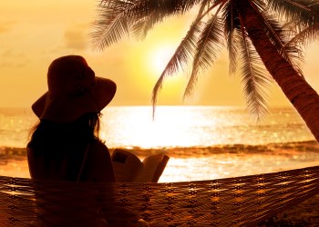 Woman reading in hammock at stunning sunset during vacation in phuket or is it Florida