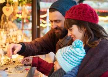 Parents show child ornaments at christmas stall.