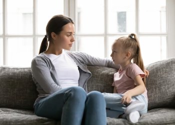 Serious young mom or nanny sit on couch with little preschooler girl talk sharing secrets, focused mother have conversation with small daughter, lecture or scold child, children upbringing concept