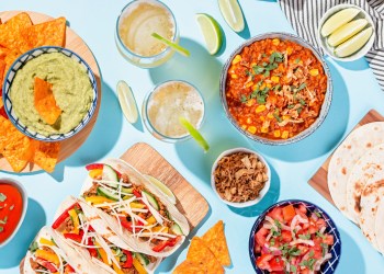 Mexican food table with traditional dishes. Chili con carne, tacos, tomato salsa, corn chips with guacamole Cinco de Mayo