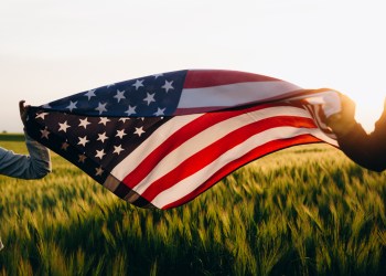Hands holding American flag in a wheat field at sunset. Independence Day, 4th of July, American Independence