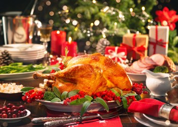 Christmas turkey dinner. Baked turkey garnished with red berries and sage leaves in front of Christmas tree and burning candles