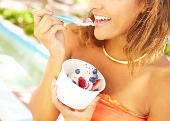 Portrait of a happy young mixed race woman enjoying frozen yogurt with blueberry and strawberry fruit toppings outside. ice cream hamptons north fork