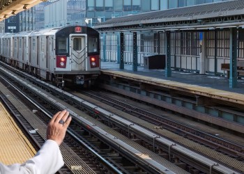 New York subway train arriving at outdoor covered platform among highrises on cold day