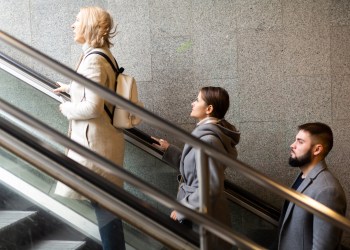 Side view of focused people coming out of underground walkway, moving up on escalator