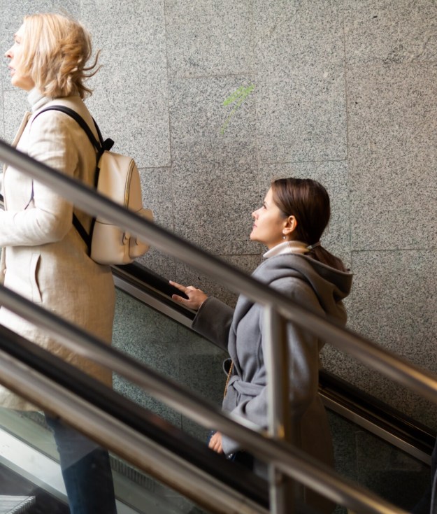 Side view of focused people coming out of underground walkway, moving up on escalator