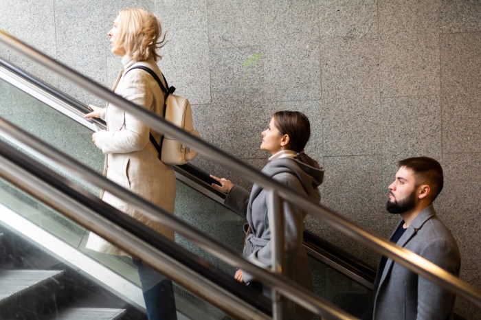 Side view of focused people coming out of underground walkway, moving up on escalator