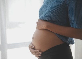 Happy pregnant woman touching belly in front of white wall - Soundview Pregnancy Services helps women make choices