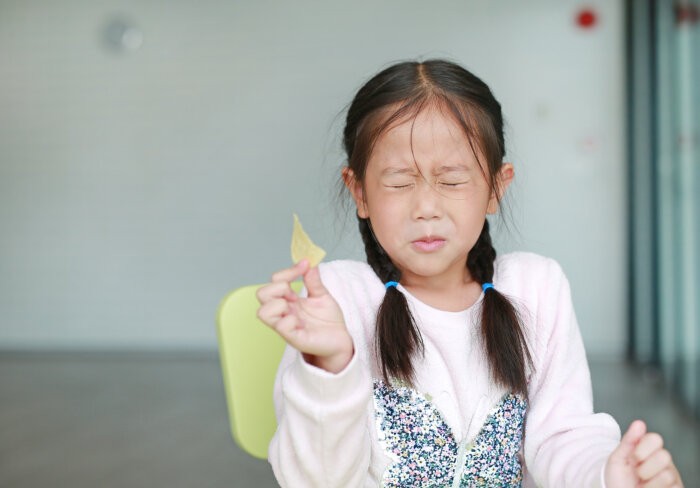 Portraits of cute Asian little girl eating crispy potato chips with face emotion feeling sour. kids