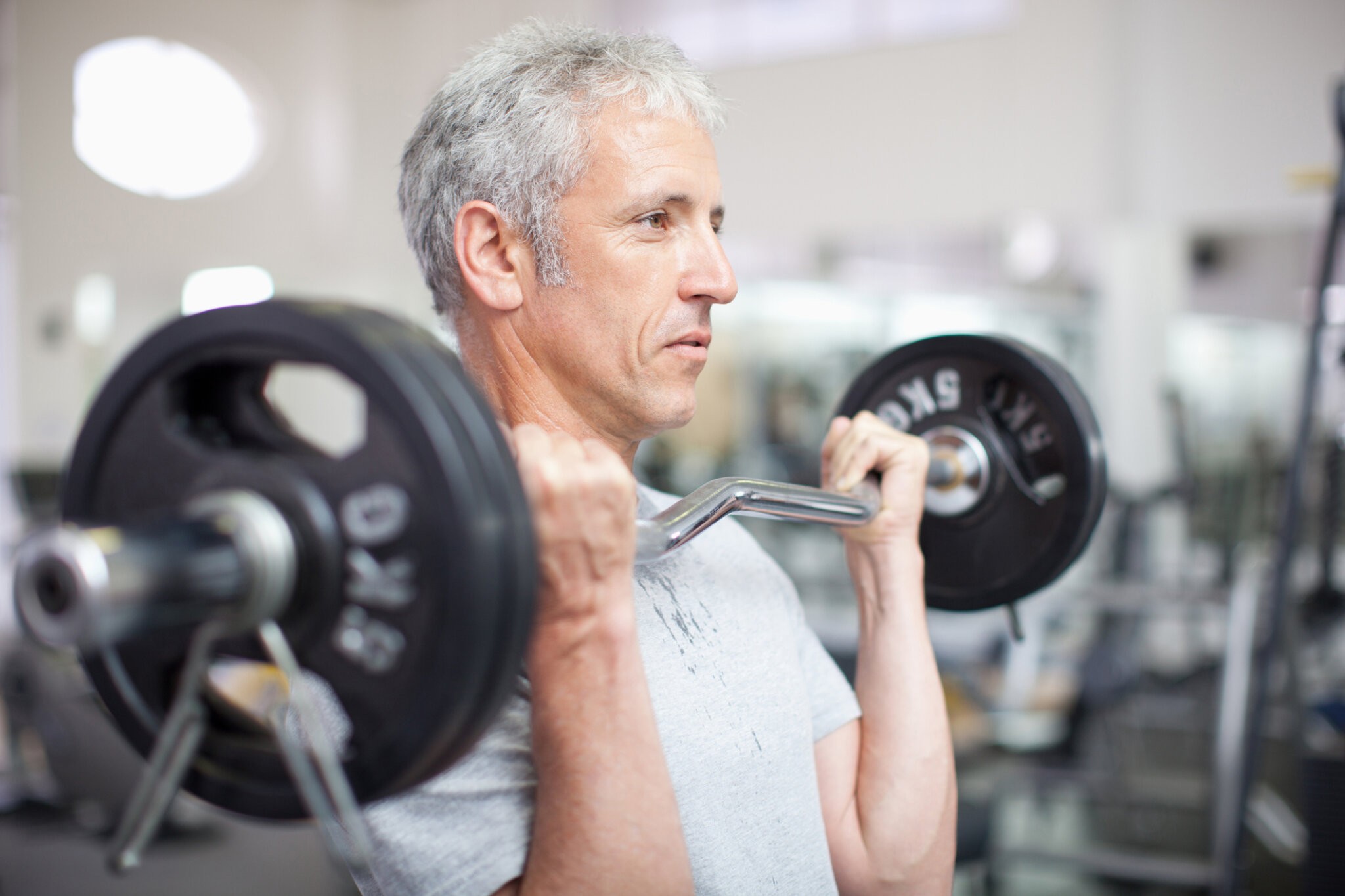 Portrait of smiling aging man holding barbell in gymnasium