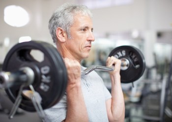 Portrait of smiling aging man holding barbell in gymnasium