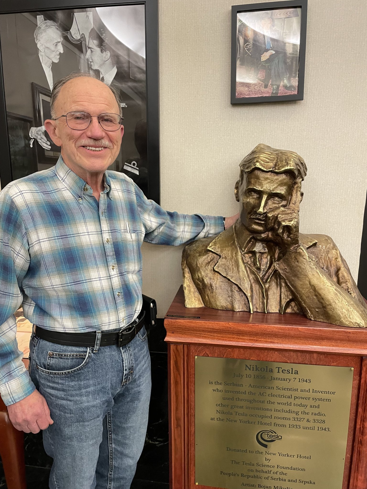 Cartoonist Joe Staton, standing with a bronze bust of Nikola Tesla on exhibit in the basement of the New Yorker Hotel.