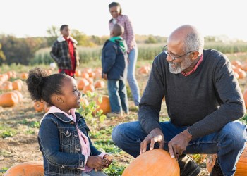 A grandfather and his granddaughter looking at pumpkins while kids are pumpkin picking