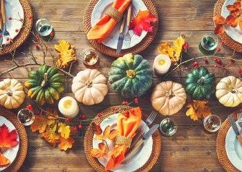 Autumnal decorated table for celebrating Thanksgiving or other family celebration. Festive table setting with plates, glassware, pumpkins, rose hip branches and leaves on wooden table background, top view